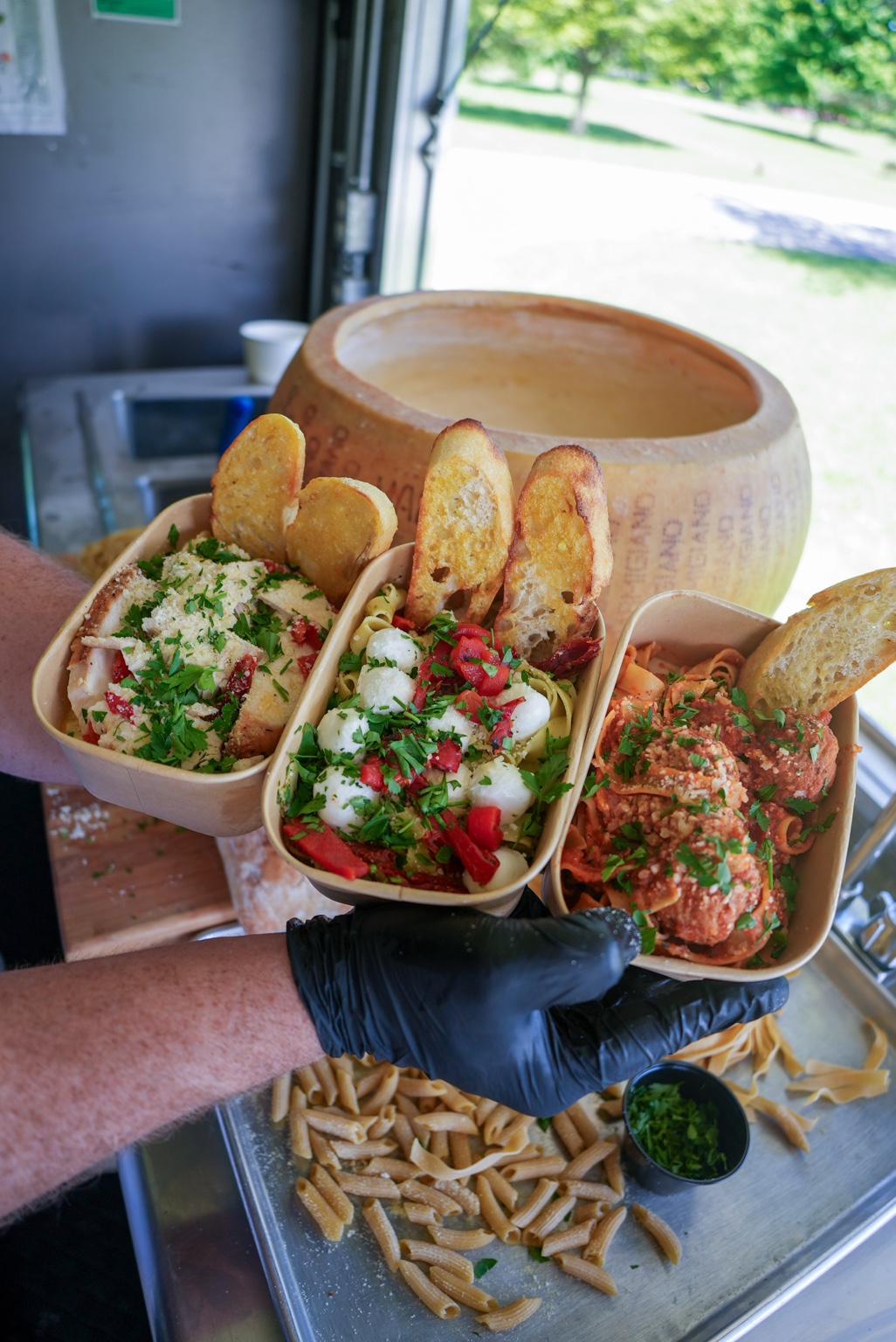 Three colorful Pasta Stop bowls beside the cheese wheel